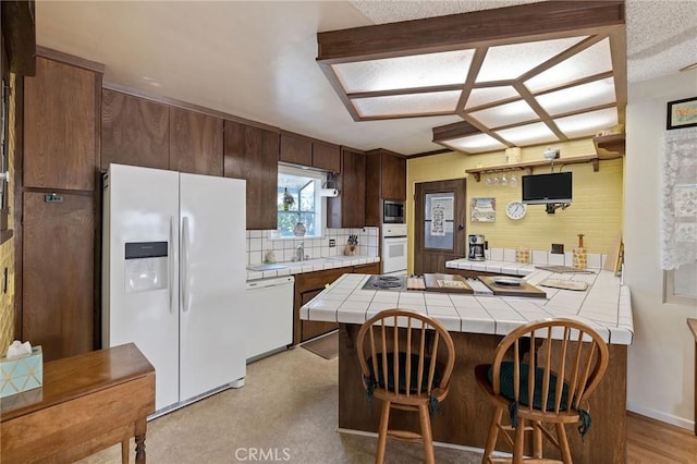 kitchen with tile countertops, kitchen peninsula, a kitchen bar, sink, and white appliances