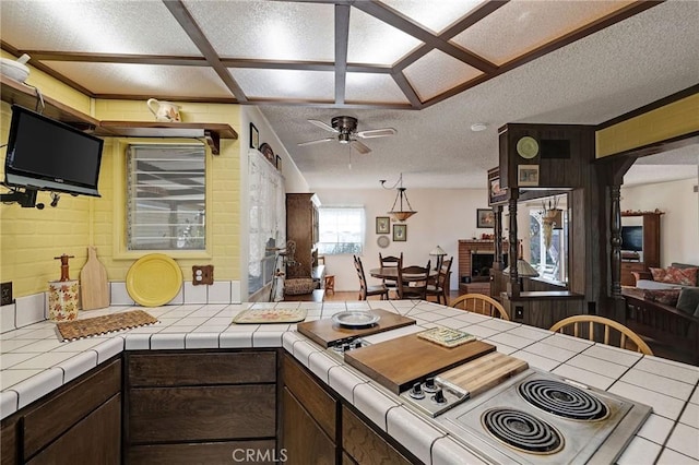 kitchen featuring a textured ceiling, tile counters, a fireplace, ceiling fan, and dark brown cabinets