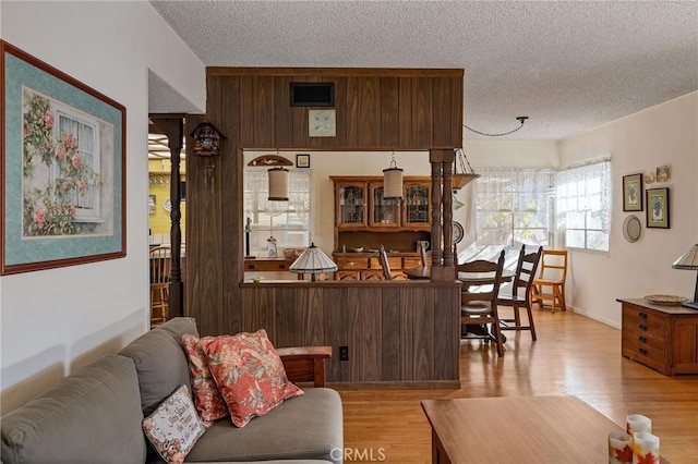 bar with light wood-type flooring, dark brown cabinets, a textured ceiling, and a notable chandelier