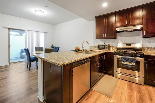 kitchen featuring kitchen peninsula, appliances with stainless steel finishes, light hardwood / wood-style flooring, light stone counters, and sink