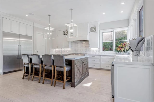 kitchen with a kitchen island, a breakfast bar, pendant lighting, white cabinetry, and stainless steel built in refrigerator