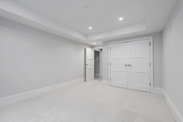 unfurnished bedroom featuring light carpet, a tray ceiling, and a closet