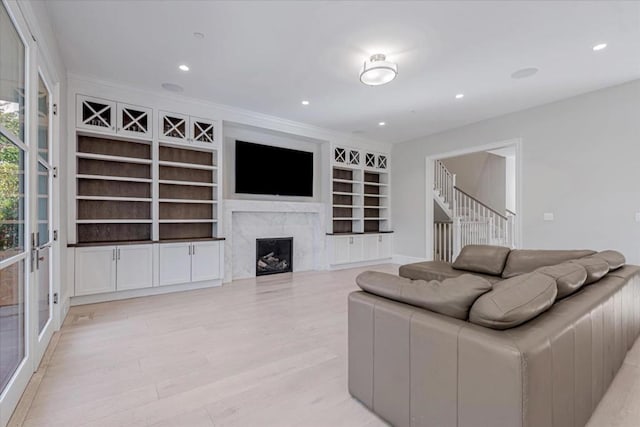 living room with a premium fireplace, built in features, and light hardwood / wood-style floors