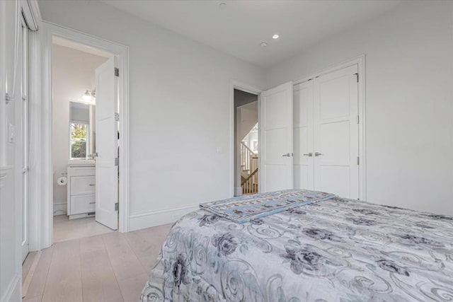 bedroom with light hardwood / wood-style flooring, ensuite bath, and a closet