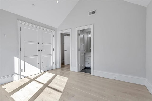 unfurnished bedroom with connected bathroom, vaulted ceiling, light hardwood / wood-style floors, and a closet