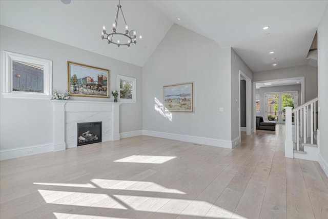 living room with a high end fireplace, an inviting chandelier, high vaulted ceiling, and light wood-type flooring