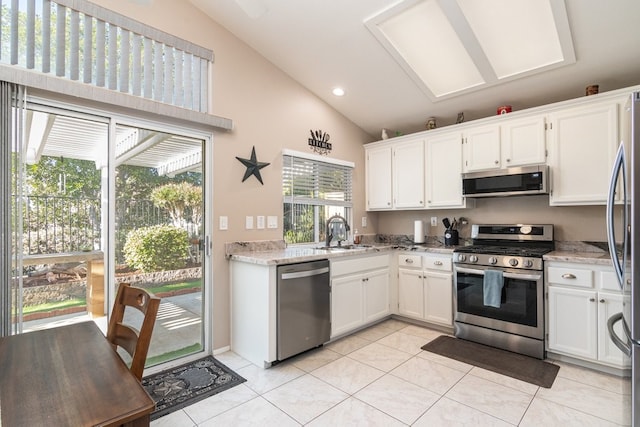 kitchen featuring vaulted ceiling, sink, light tile patterned floors, appliances with stainless steel finishes, and white cabinets