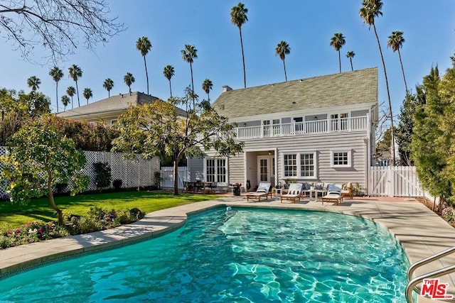 back of property with a balcony, a fenced in pool, a lawn, and a patio