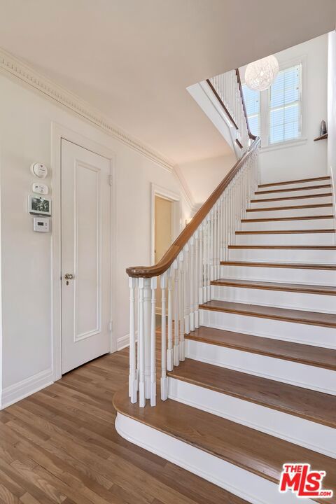 stairs featuring wood-type flooring, ornamental molding, and an inviting chandelier