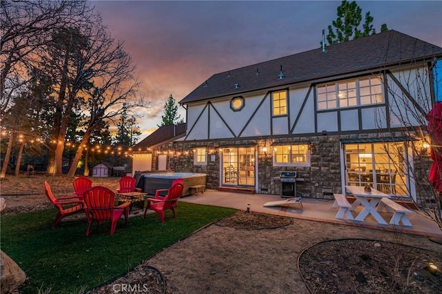 back house at dusk featuring a hot tub and a patio