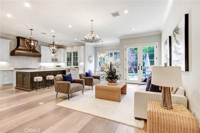 living room with french doors, an inviting chandelier, ornamental molding, and light hardwood / wood-style floors