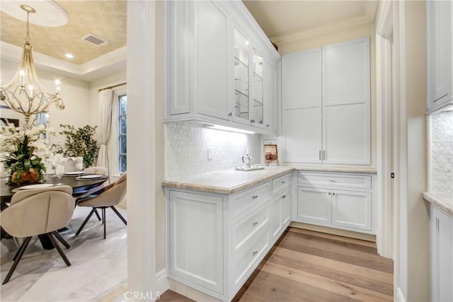 kitchen with backsplash, a notable chandelier, pendant lighting, light hardwood / wood-style flooring, and white cabinets