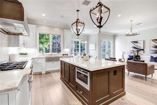 kitchen featuring stainless steel microwave, a center island, pendant lighting, sink, and white cabinets