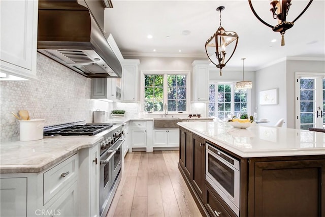 kitchen with extractor fan, a center island, appliances with stainless steel finishes, white cabinets, and a chandelier