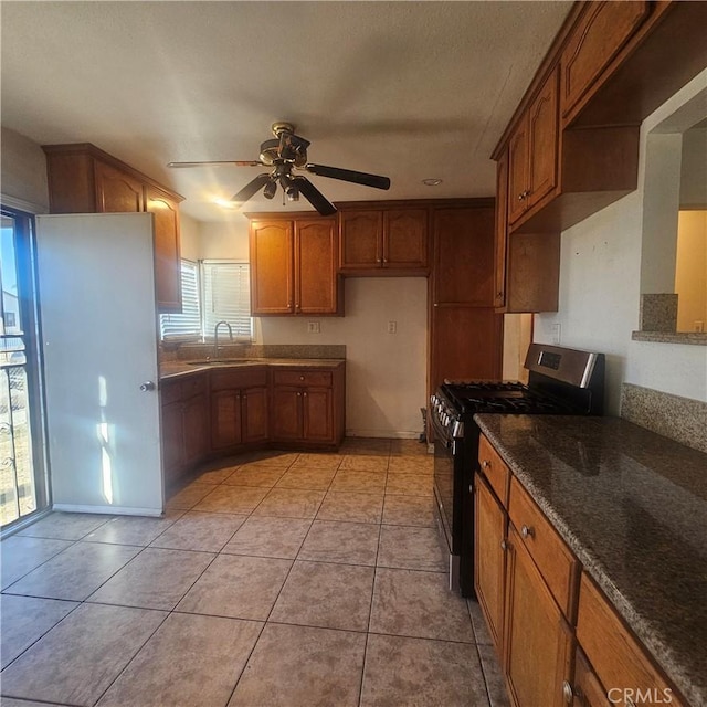 kitchen featuring light tile patterned floors, stainless steel gas range oven, ceiling fan, dark stone counters, and sink