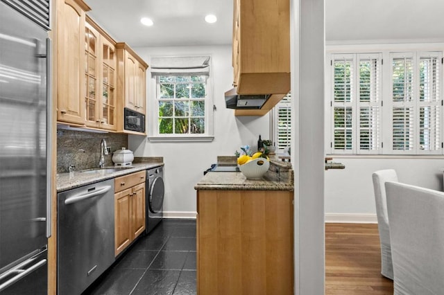 kitchen featuring washer / dryer, sink, built in appliances, plenty of natural light, and light stone countertops