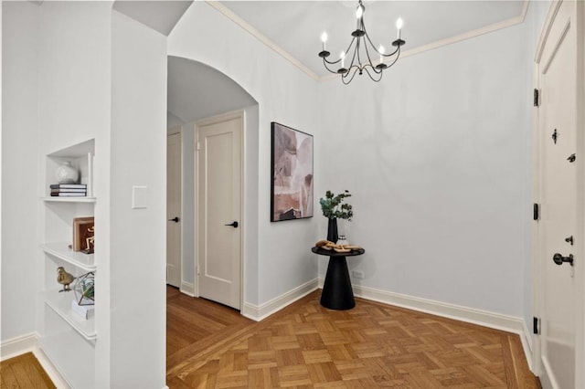 hall featuring a notable chandelier, built in shelves, ornamental molding, and light parquet flooring