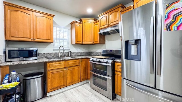 kitchen featuring appliances with stainless steel finishes, light hardwood / wood-style flooring, stone countertops, and sink