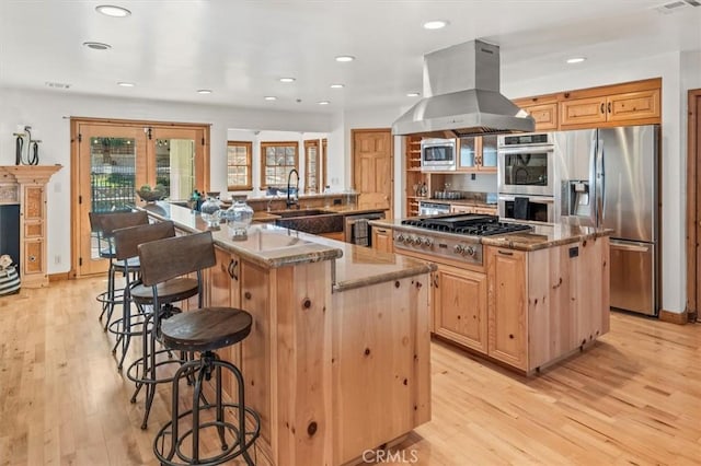 kitchen with dark stone countertops, island range hood, a spacious island, light wood-style floors, and appliances with stainless steel finishes