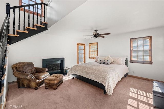 carpeted bedroom featuring a glass covered fireplace, ceiling fan, and baseboards