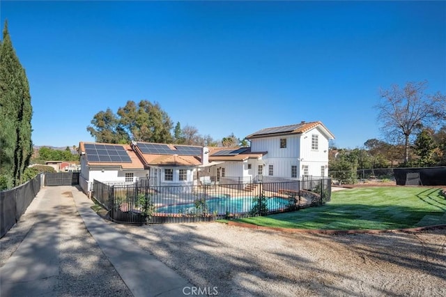 view of front facade featuring a fenced backyard, a fenced in pool, roof mounted solar panels, a patio area, and a front lawn