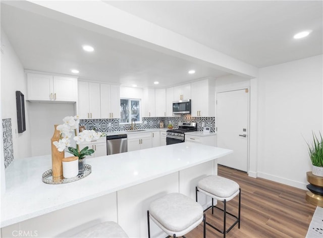 kitchen with decorative backsplash, kitchen peninsula, white cabinets, and stainless steel appliances