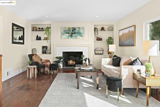 living room with built in shelves, a brick fireplace, and dark hardwood / wood-style floors