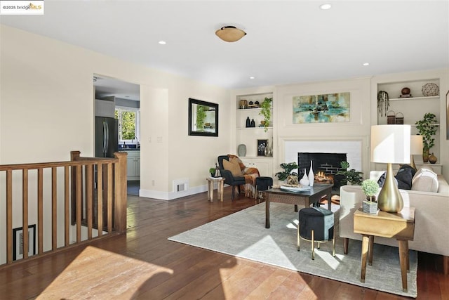 living room with dark wood-type flooring, built in features, and a fireplace