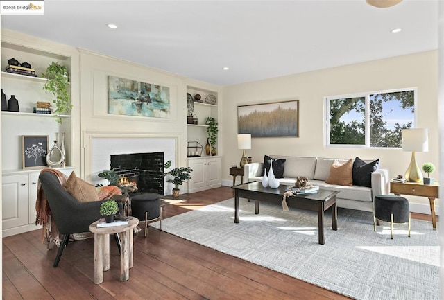 living room with dark wood-type flooring, built in shelves, and a fireplace