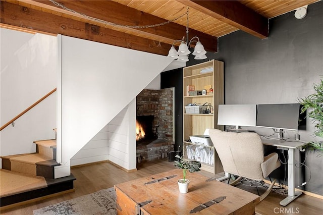 home office featuring a brick fireplace, a notable chandelier, beamed ceiling, light hardwood / wood-style flooring, and wooden ceiling