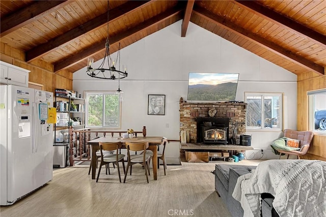 dining area featuring a brick fireplace, beamed ceiling, a chandelier, and wooden ceiling