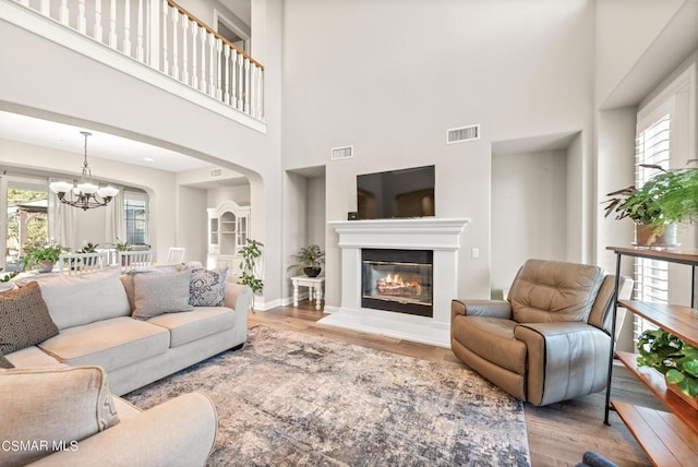 living room with a notable chandelier, a towering ceiling, and light wood-type flooring