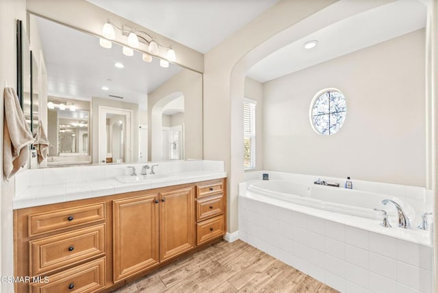 bathroom with tiled tub, vanity, and hardwood / wood-style flooring