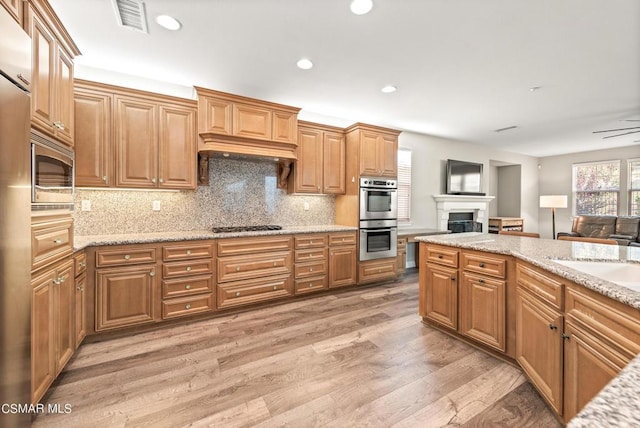 kitchen featuring ceiling fan, stainless steel appliances, light stone counters, wood-type flooring, and decorative backsplash