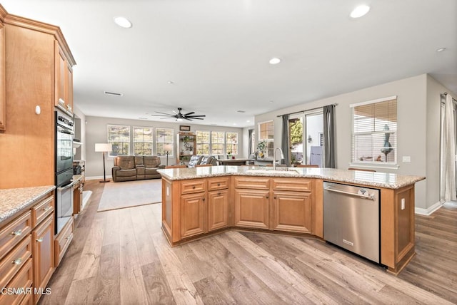 kitchen with ceiling fan, stainless steel appliances, light stone counters, light hardwood / wood-style floors, and an island with sink