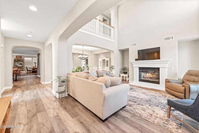 living room featuring an inviting chandelier, a towering ceiling, and light hardwood / wood-style floors