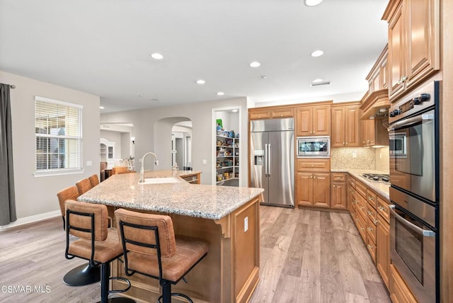 kitchen featuring tasteful backsplash, sink, built in appliances, light stone countertops, and a center island with sink