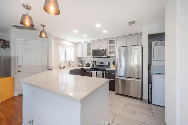 kitchen with stacked washing maching and dryer, appliances with stainless steel finishes, decorative light fixtures, sink, and kitchen peninsula