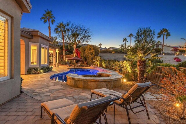 patio terrace at dusk featuring a pool with hot tub