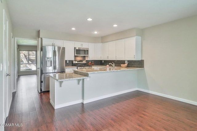 kitchen featuring white cabinetry, kitchen peninsula, stainless steel appliances, decorative backsplash, and light stone counters