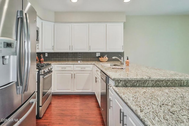 kitchen featuring appliances with stainless steel finishes, backsplash, dark wood-type flooring, white cabinets, and sink