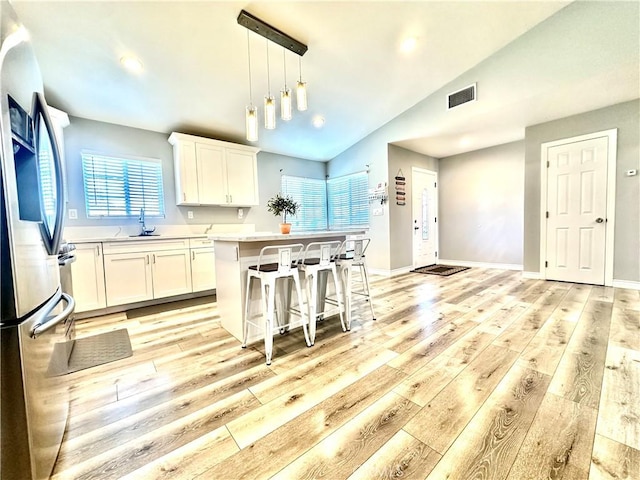 kitchen with vaulted ceiling, white cabinetry, sink, and stainless steel refrigerator