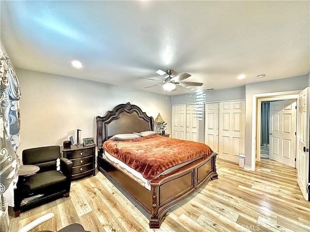 bedroom featuring ceiling fan, light hardwood / wood-style floors, and two closets