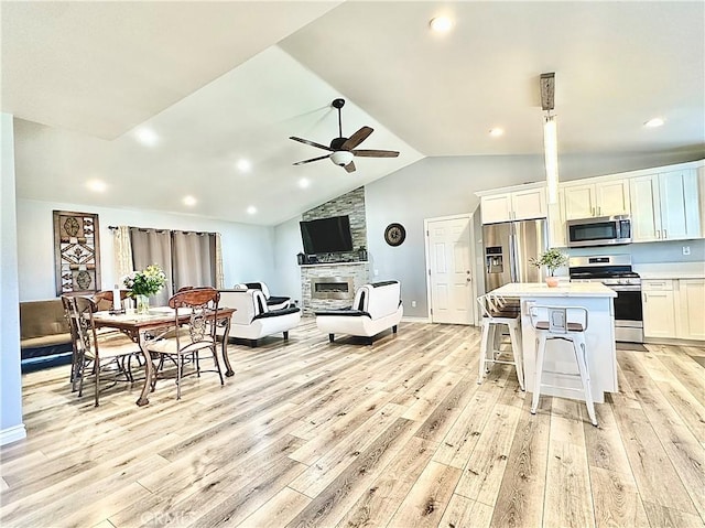 living room featuring vaulted ceiling, ceiling fan, light hardwood / wood-style floors, and a stone fireplace