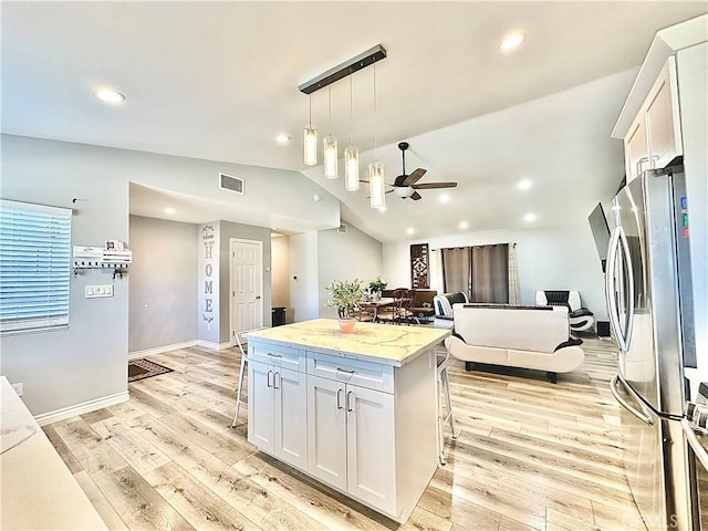 kitchen with lofted ceiling, ceiling fan, a center island, stainless steel refrigerator, and white cabinets