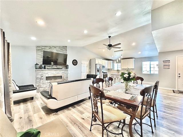 dining room featuring vaulted ceiling, ceiling fan, a fireplace, and light hardwood / wood-style flooring