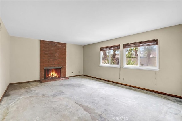 unfurnished living room featuring a brick fireplace, baseboards, and unfinished concrete flooring