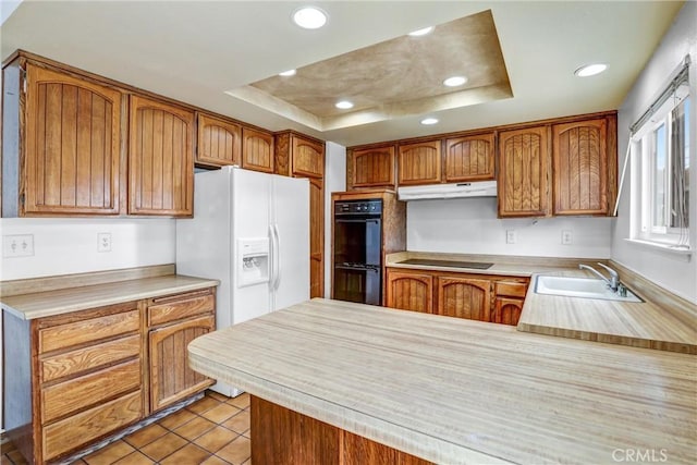 kitchen with under cabinet range hood, a peninsula, light countertops, black appliances, and a raised ceiling