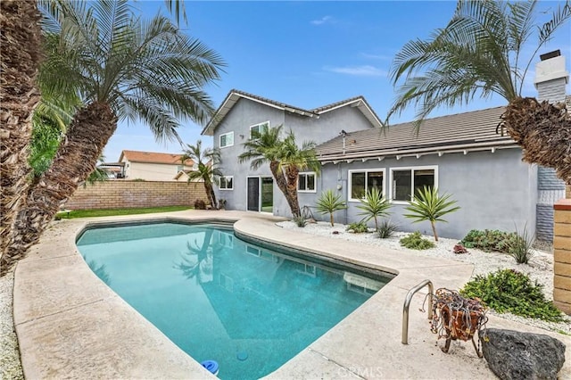 rear view of property featuring fence, a fenced in pool, and stucco siding