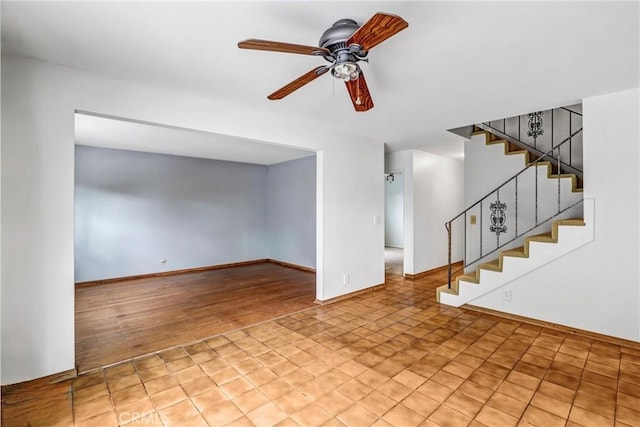 spare room with light wood-type flooring, ceiling fan, stairs, and baseboards